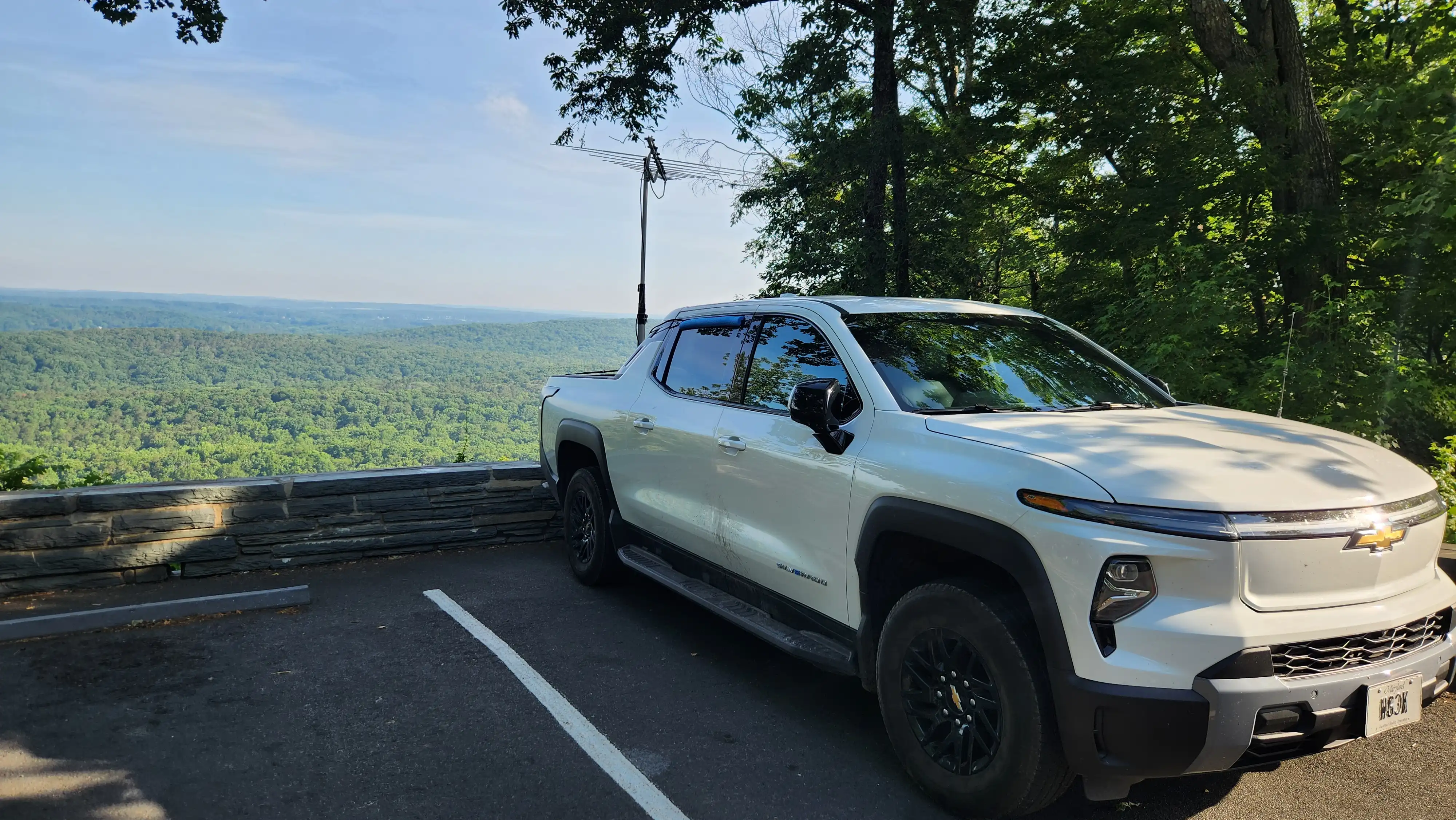 A white pickup truck with a log periodic antenna mounted on the back parked at the summit of Morrow Mountain with a view of the valley below.